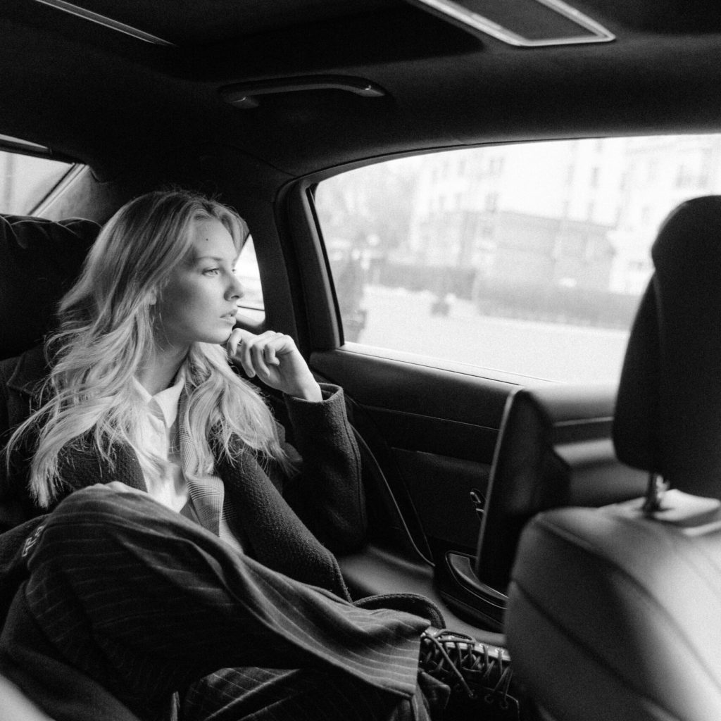 Black and white image of a thoughtful businesswoman sitting in a luxury car, exuding professionalism.