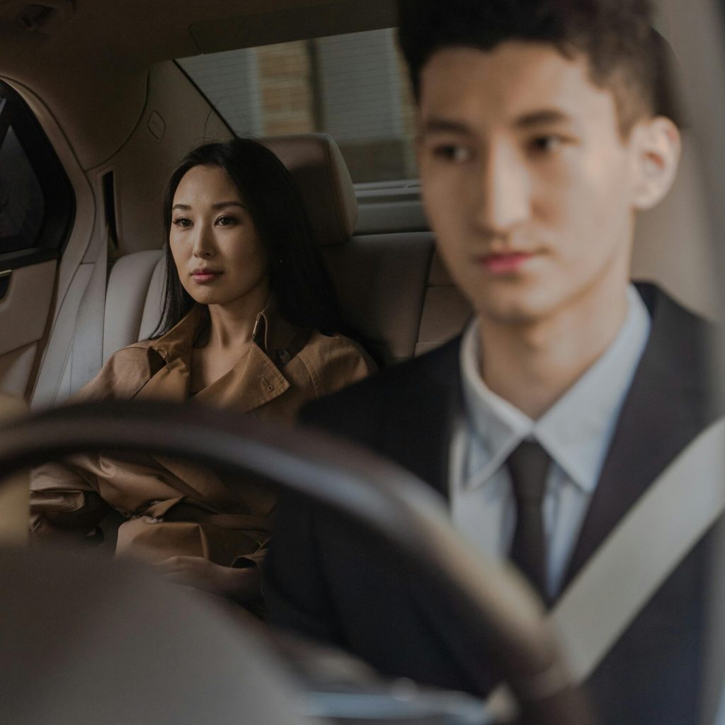 A professional driver navigates a luxury car with an elegant passenger in the back seat.